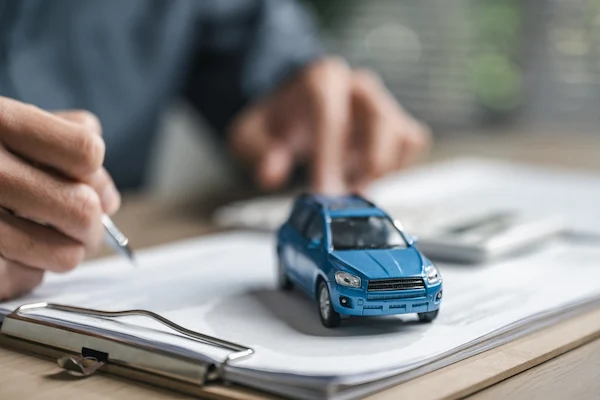 Toy car on paperwork with a driver buying auto insurance after an accident.