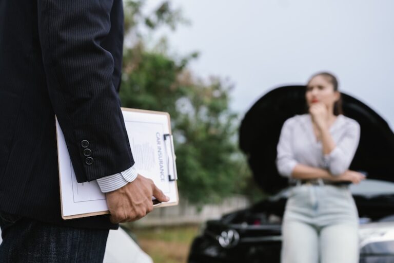 An insurance agent is holding a clipboard discussing car accident claims with a concerned vehicle owner at the accident scene in North Carolina.