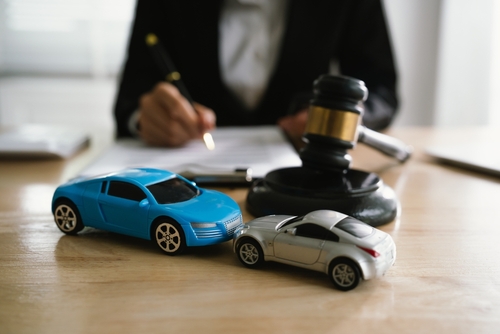 Car crash victim sitting at table with two cars and a gavel seeking help from car accident lawyer on what legal steps to take after a car accident.