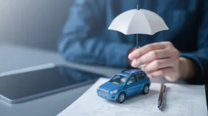 A hand holds a small white umbrella over a blue toy SUV resting on top of a printed document beside a tablet and pen visually representing the financial protection that car insurance claims provide to policyholders after an accident with help from Mogy Law in North Carolina.