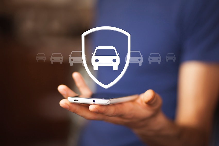 A person holds a smartphone displaying a glowing digital shield icon with a car graphic surrounded by smaller vehicle icons illustrating the mobile technology modern drivers use to manage and file car insurance claims from anywhere in North Carolina.